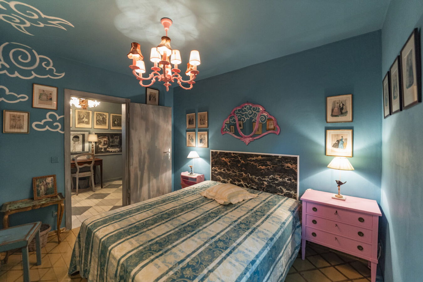 Bunt eingerichtetes Schlafzimmer mit blaugrünen Wänden, Doppelbett, Kronleuchter und pinken Nachttischen
