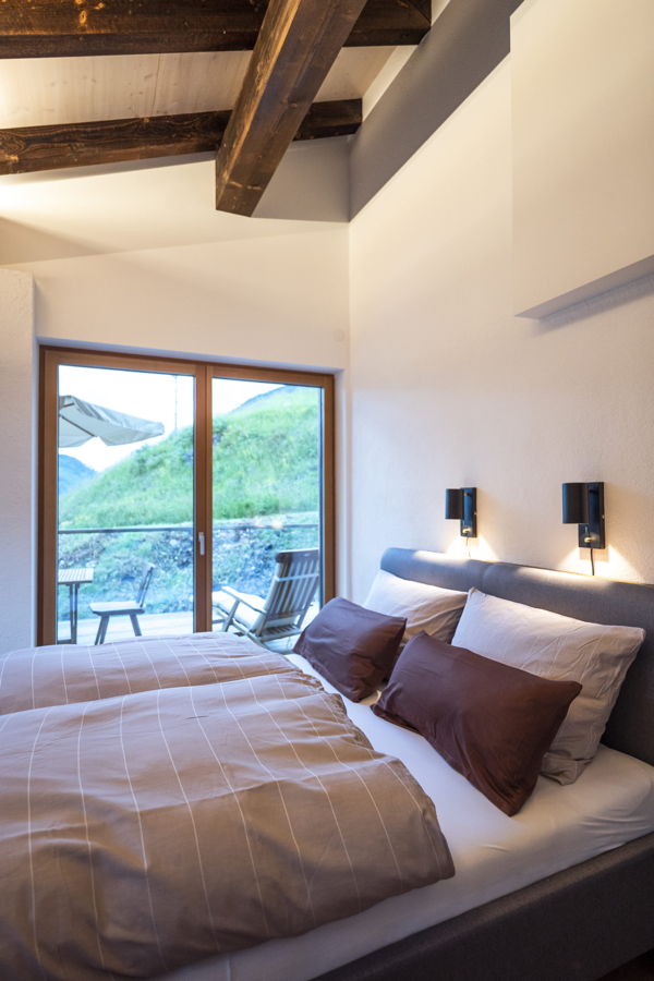 Gemütliches Schlafzimmer mit Doppelbett, Holzbalkendecke und Blick auf eine Terrasse mit Berglandschaft