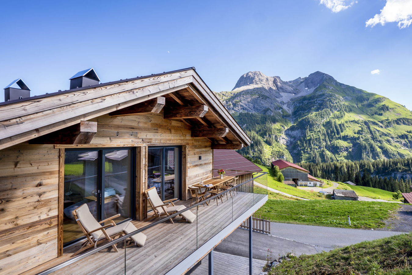Restaurant, Hotel, Ferienhaus Holzchalet mit Balkon und Liegestühlen vor einer grünen Berglandschaft