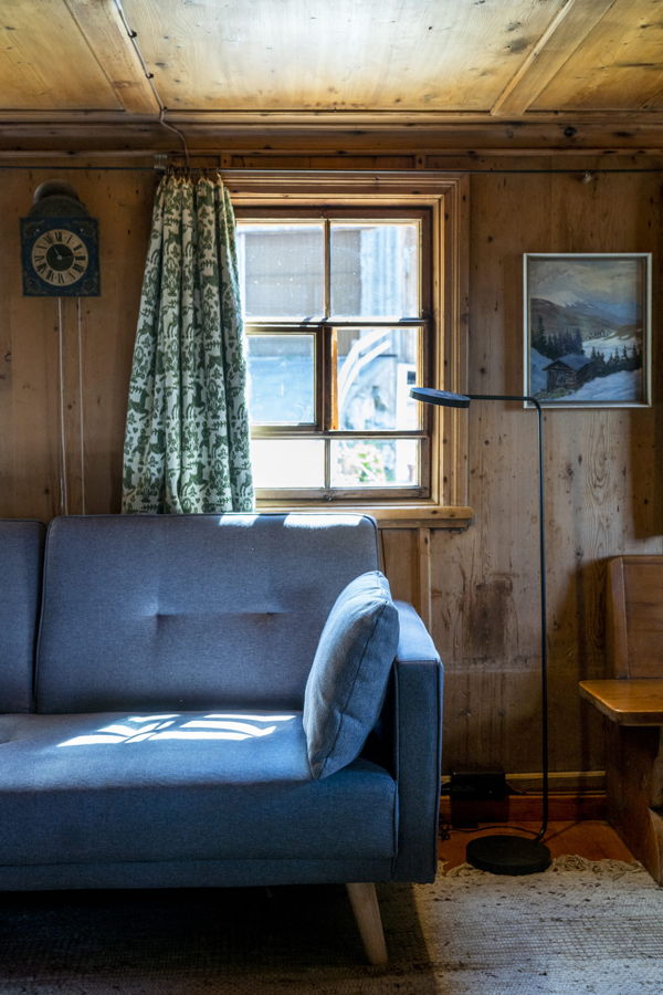 Gemütliches Wohnzimmer mit blauem Sofa, Fenster, Stehlampe und Holzvertäfelung