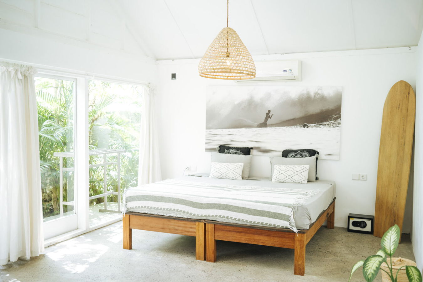 Helles Schlafzimmer mit Holzbett, großen Fenstern und Surfbrett an der Wand