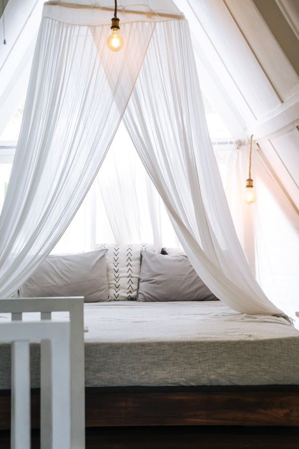 Bett mit weißem Baldachin und hängenden Glühbirnen in einem hellen Zimmer