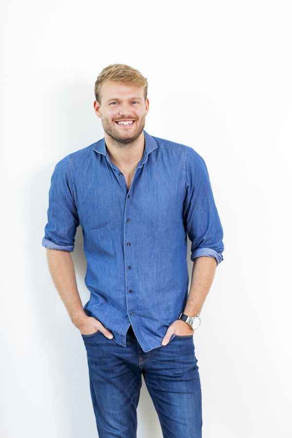 Mann in blauem Hemd und Jeans, lächelnd vor weißem Hintergrund