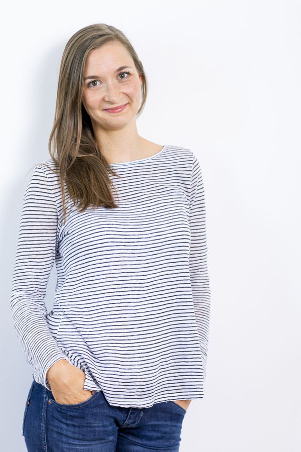 Porträt einer lächelnden Frau in gestreiftem Langarmshirt und Jeans vor hellem Hintergrund