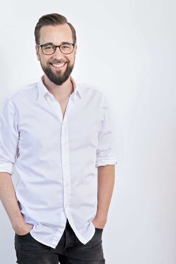 Porträt eines lächelnden Mannes mit Brille und weißem Hemd vor hellem Hintergrund