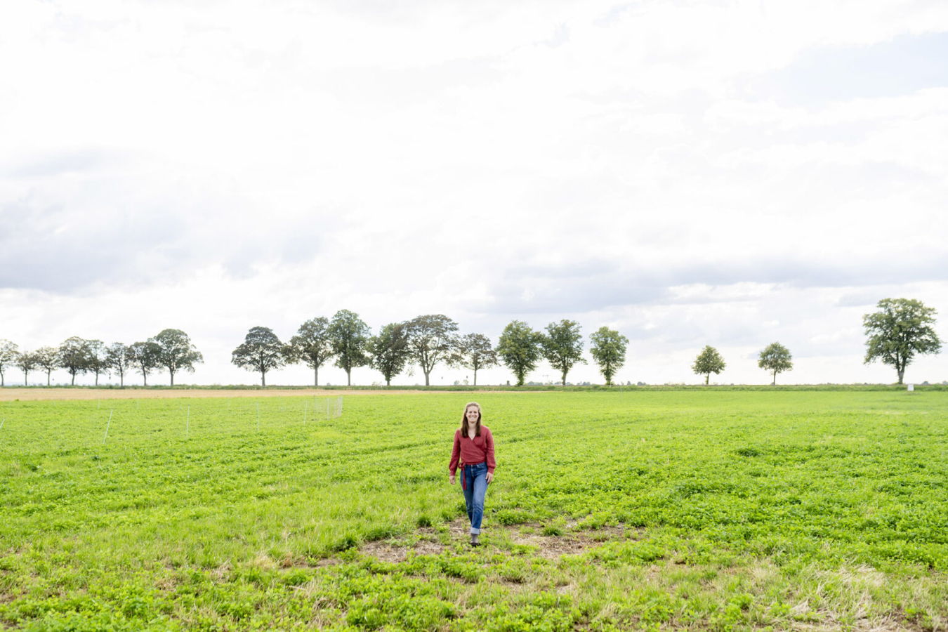 Frau geht über ein grünes Feld unter bewölktem Himmel