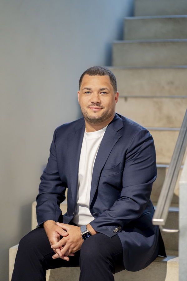 Mann im dunkelblauen Blazer und weißem T-Shirt sitzt auf einer Treppe