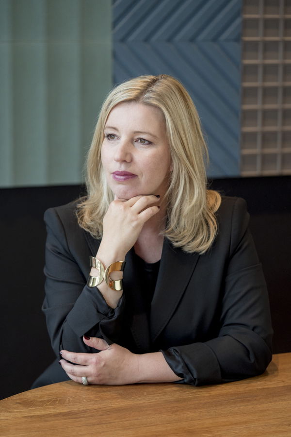 Porträt einer Frau im schwarzen Blazer, die nachdenklich am Tisch sitzt