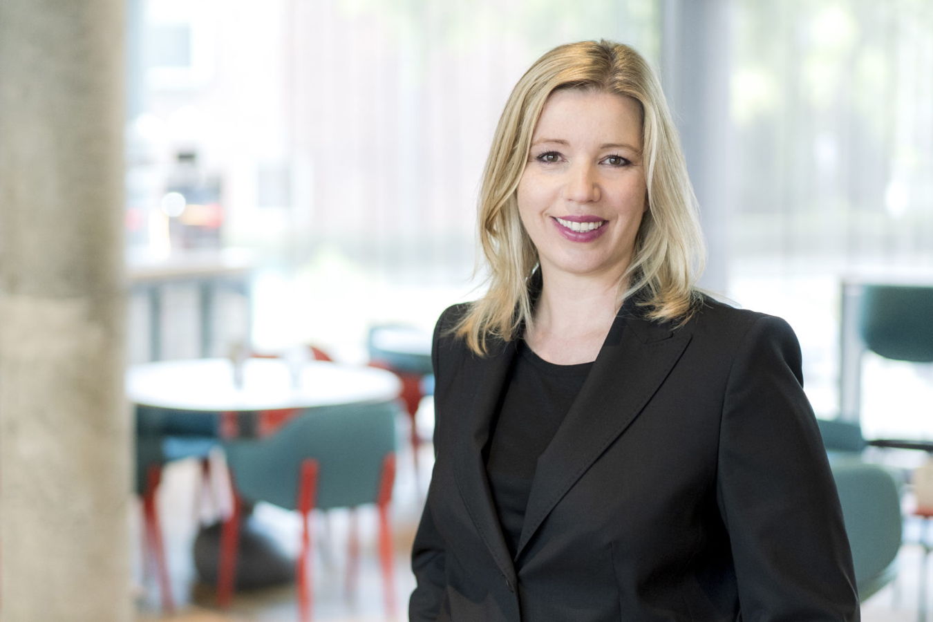 Porträt einer lächelnden Frau im schwarzen Blazer in einem modernen Innenraum