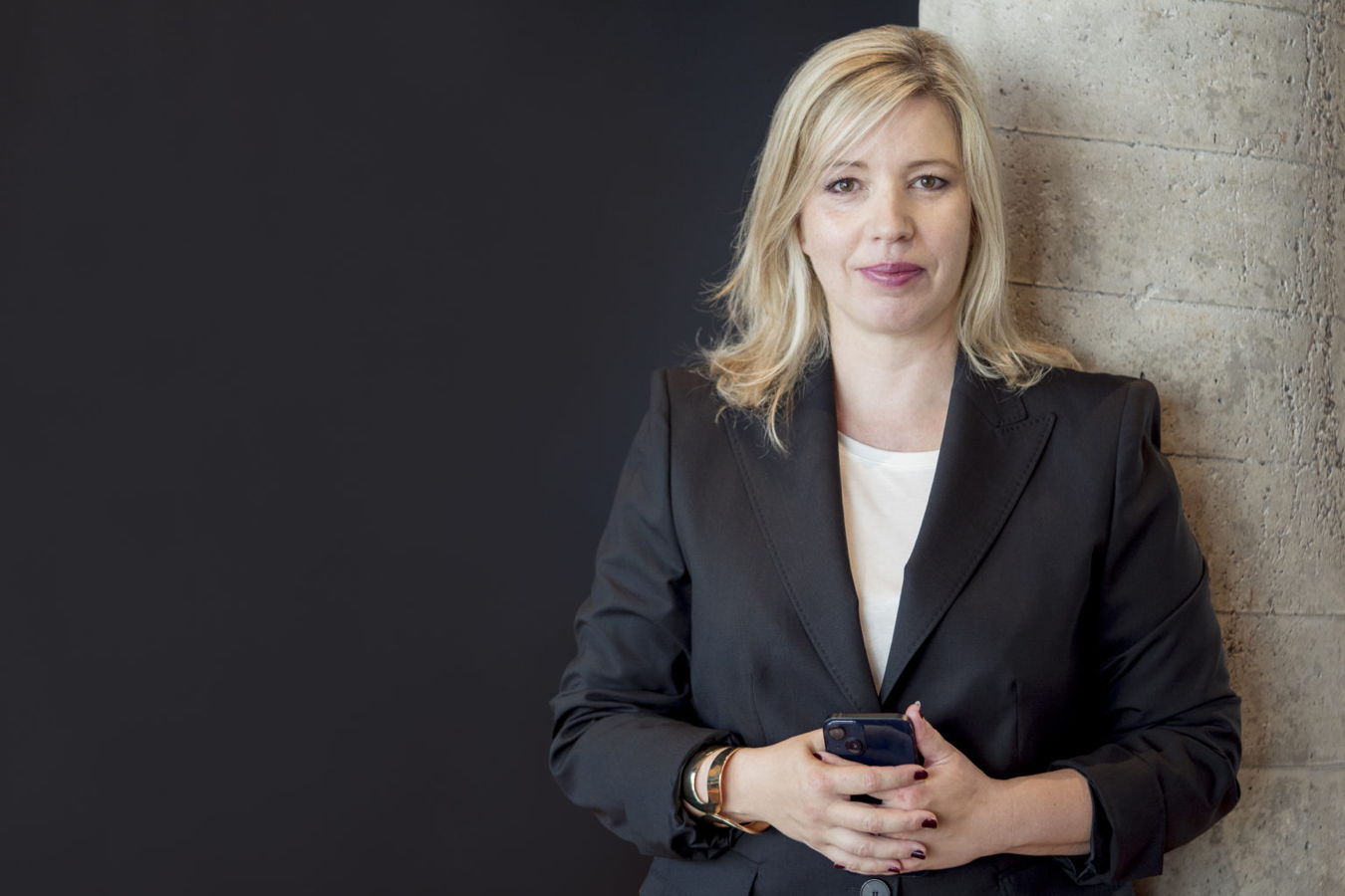 Porträt einer Frau im schwarzen Blazer, die ein Smartphone hält