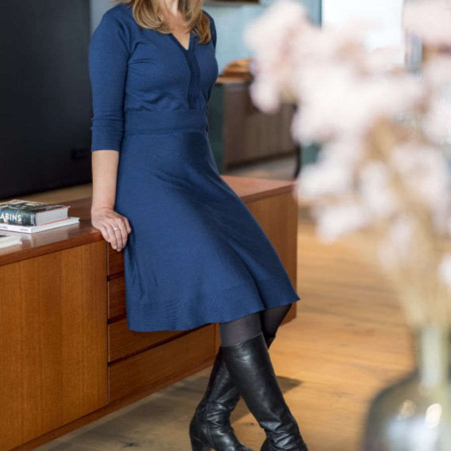 Frau in blauem Kleid lehnt an einem Holztisch in einem modernen Raum