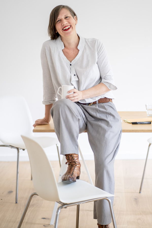 Frau sitzt lächelnd auf einem Tisch und hält eine Tasse in der Hand