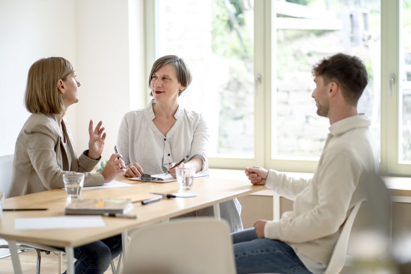 Drei Personen sitzen an einem Tisch und unterhalten sich in einem hellen Besprechungsraum