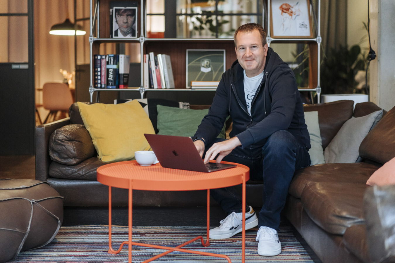 Mann sitzt auf einem Sofa und arbeitet am Laptop in einem Wohnzimmer