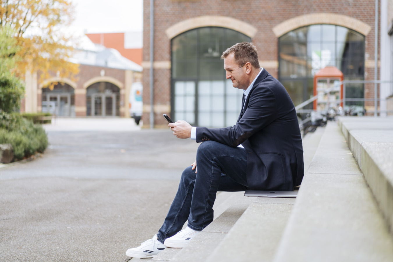 Mann im Anzug sitzt draußen auf einer Treppe und schaut auf sein Smartphone