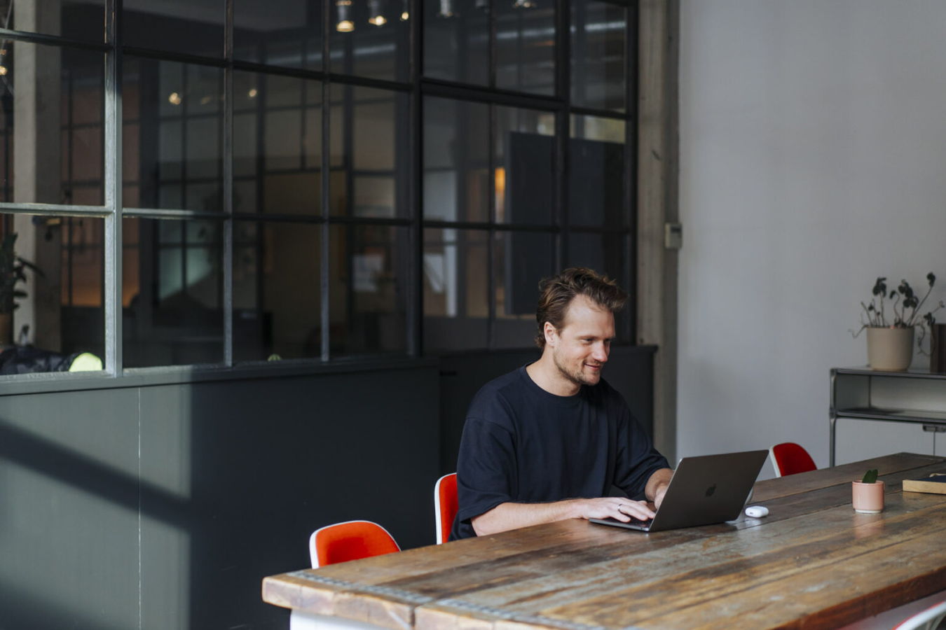 Mann arbeitet an einem Laptop an einem Holztisch in einem modernen Büro