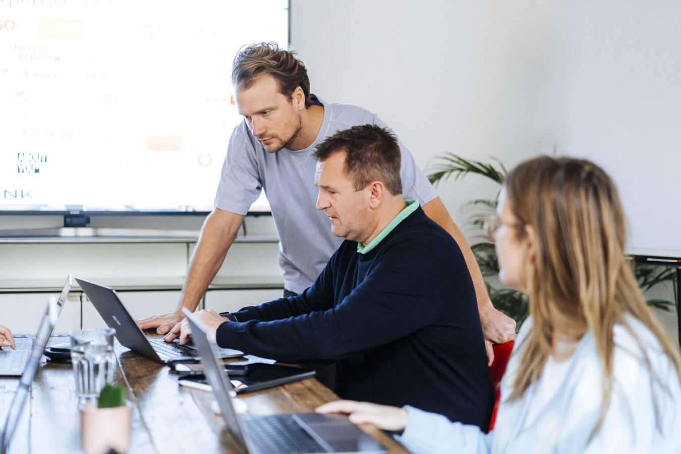 Drei Personen arbeiten gemeinsam an Laptops in einem Besprechungsraum