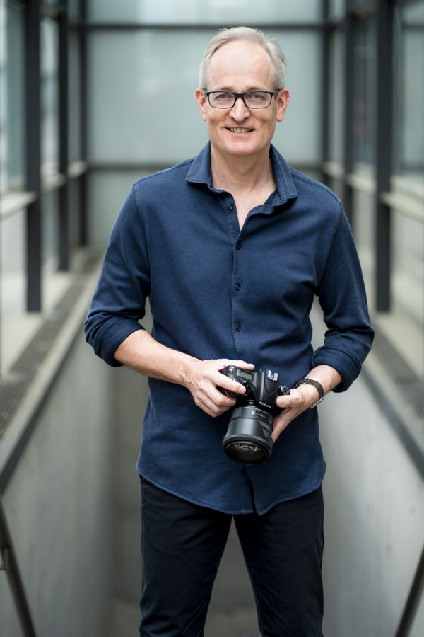 Mann mit Brille hält eine Kamera in einem modernen Gang