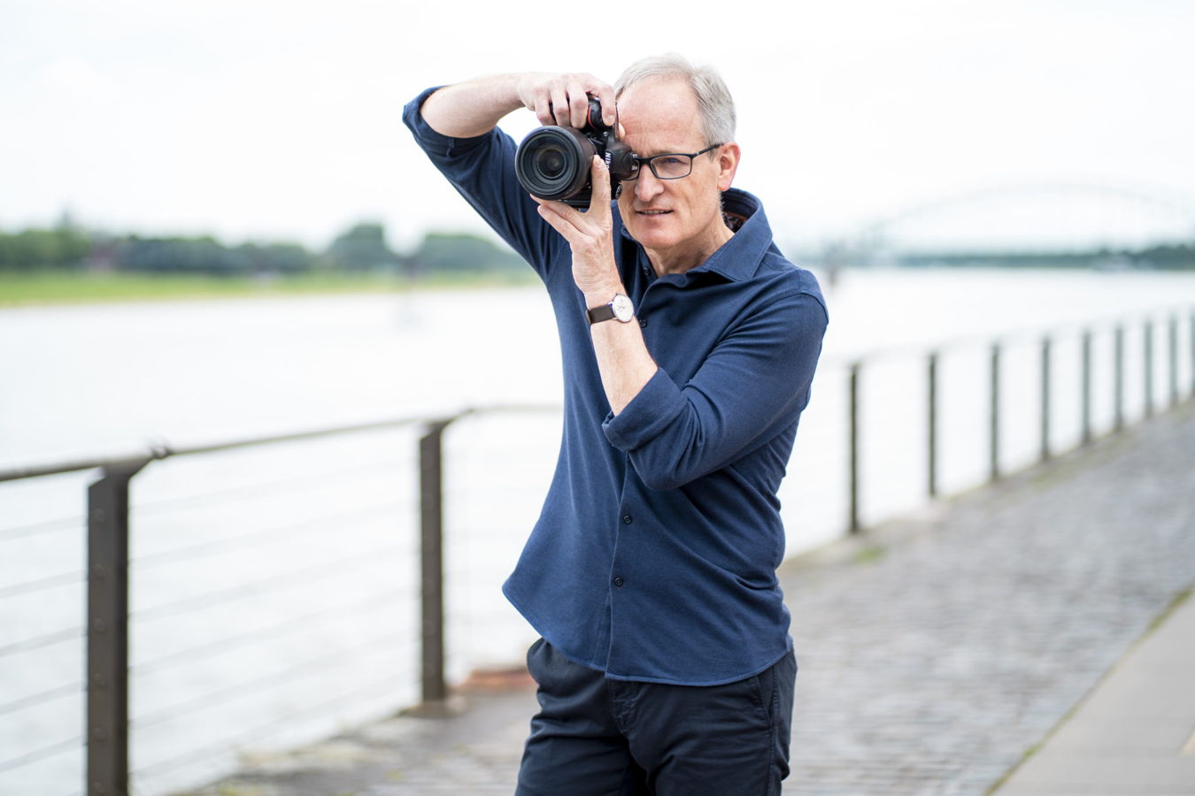 Mann fotografiert mit einer Kamera am Ufer eines Flusses