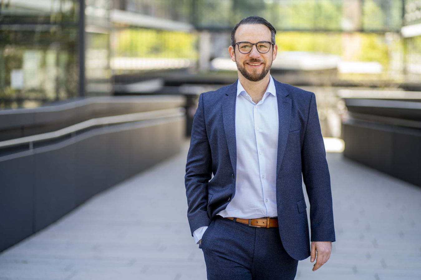 Mann im blauen Anzug und mit Brille steht lächelnd im Freien