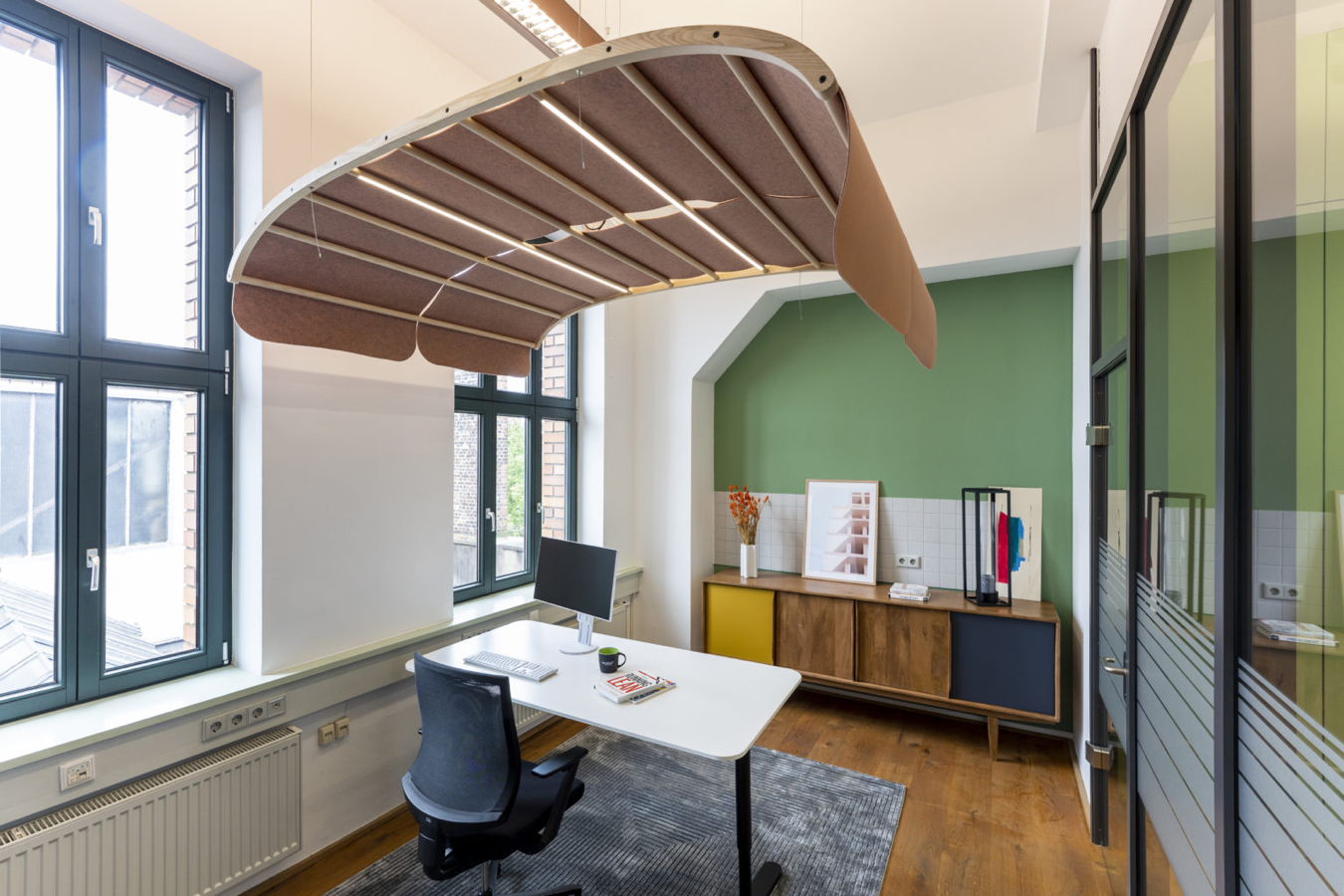 Modernes Büro mit Schreibtisch, Monitor und auffälliger hängender Akustikdecke
