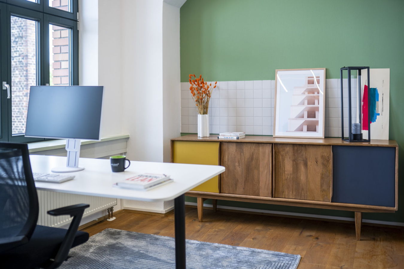 Modernes Büro mit Schreibtisch, Monitor und Sideboard vor grüner Wand