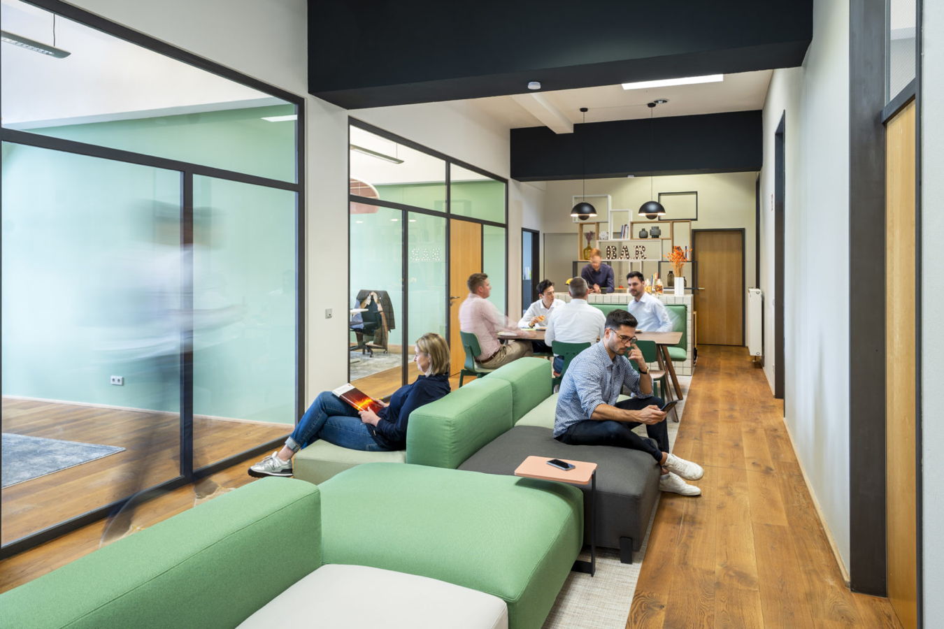 Büro-Lounge mit mehreren Personen, die an Tischen und auf Sofas arbeiten oder sich unterhalten