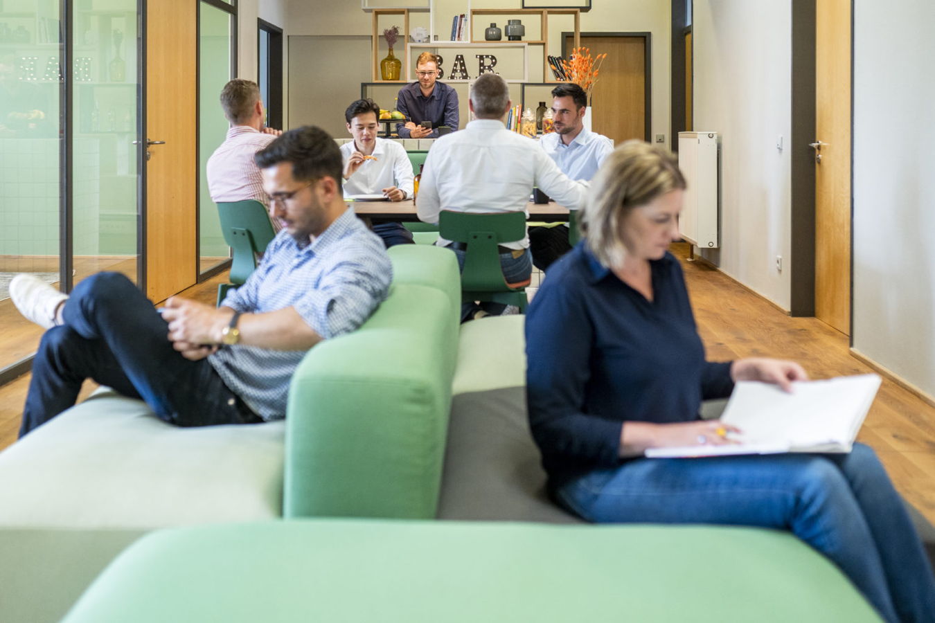 Menschen arbeiten und entspannen in einer modernen Bürolounge mit Sitzgruppen und Barbereich