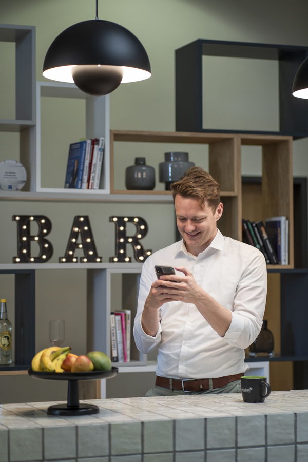 Mann in weißem Hemd tippt auf seinem Smartphone hinter einer Bar
