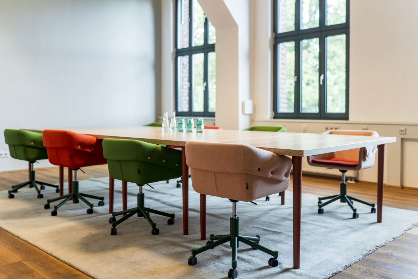 Konferenzraum mit großem Tisch und bunten Stühlen auf einem Teppich