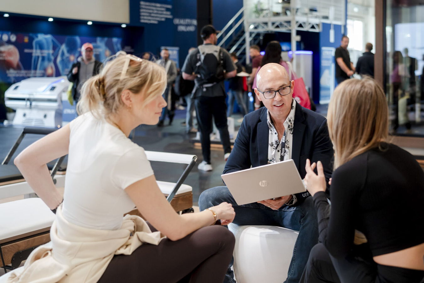 Drei Personen unterhalten sich auf einer Messe; ein Mann hält einen Laptop