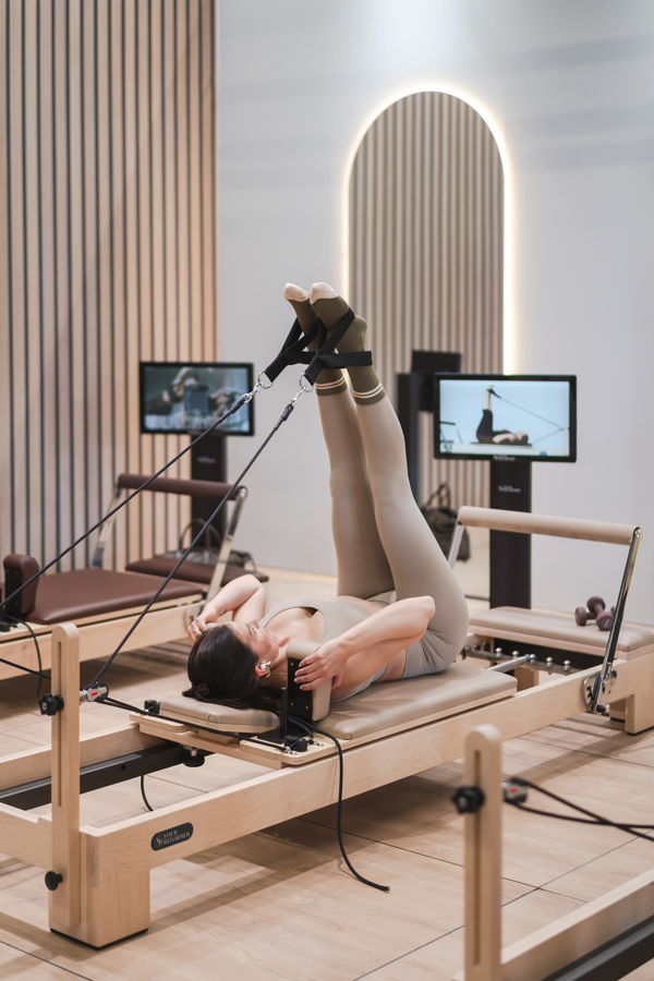 Frau trainiert auf einem Pilates-Reformer mit hochgestreckten Beinen