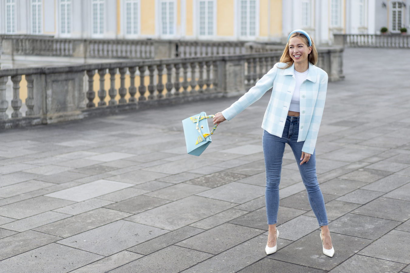 Frau in hellblauer Jacke hält eine hellblaue Einkaufstasche auf einem Platz