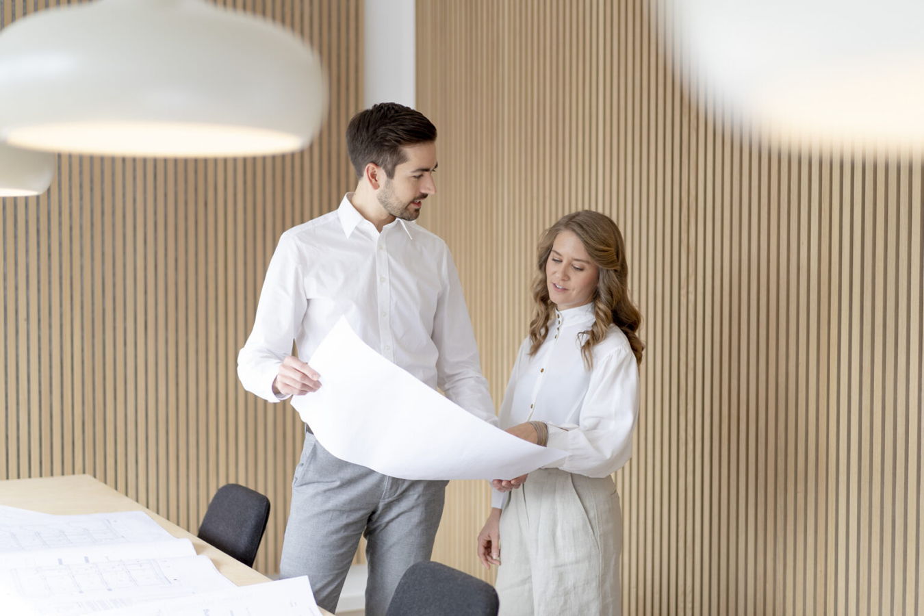 Zwei Personen besprechen einen großen Bauplan im Büro