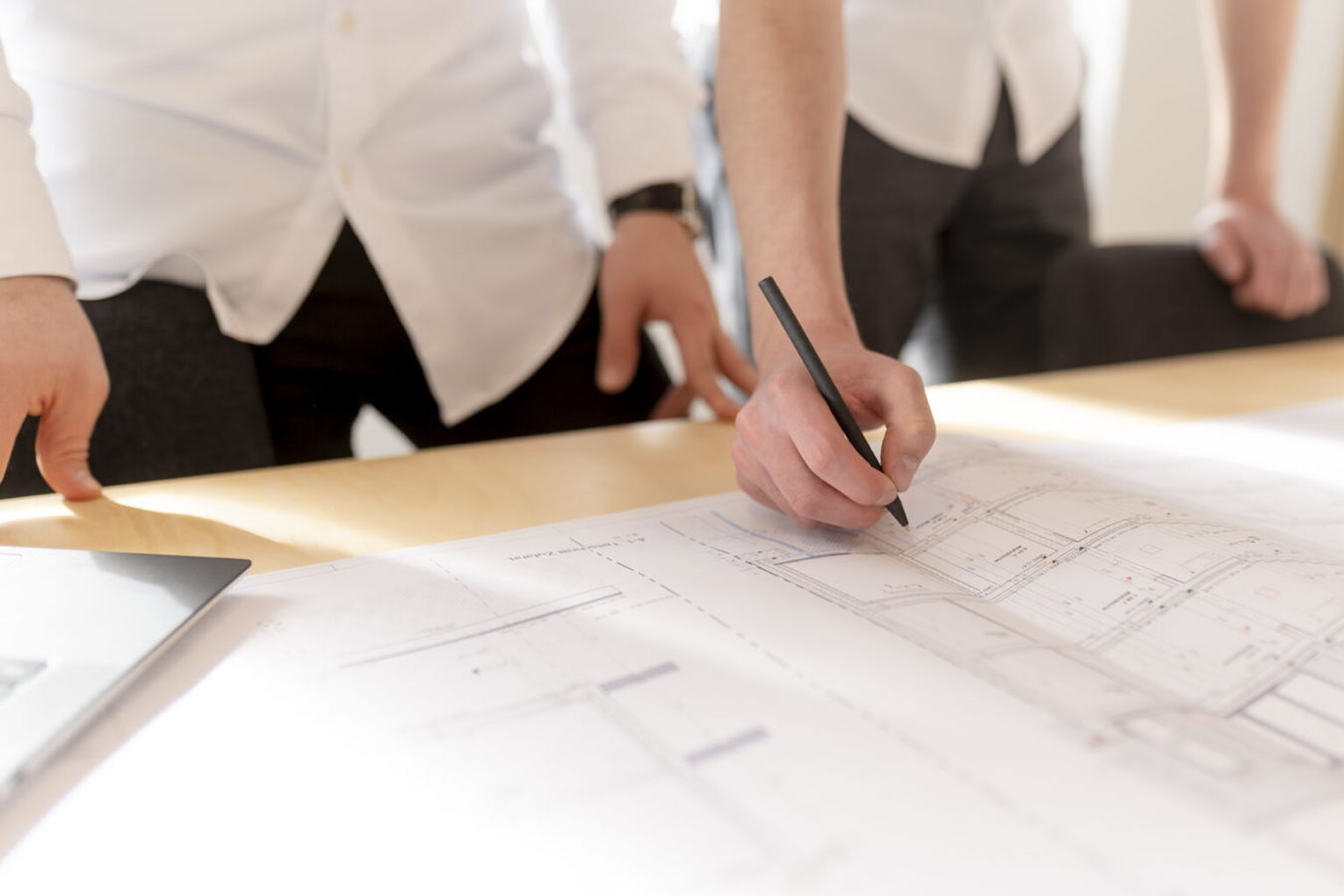 Personen prüfen Baupläne an einem Tisch und markieren Details mit einem Stift