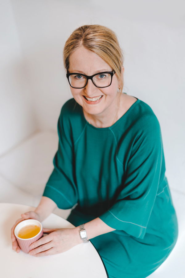 Lächelnde Frau mit Brille in grünem Kleid, die eine Tasse hält