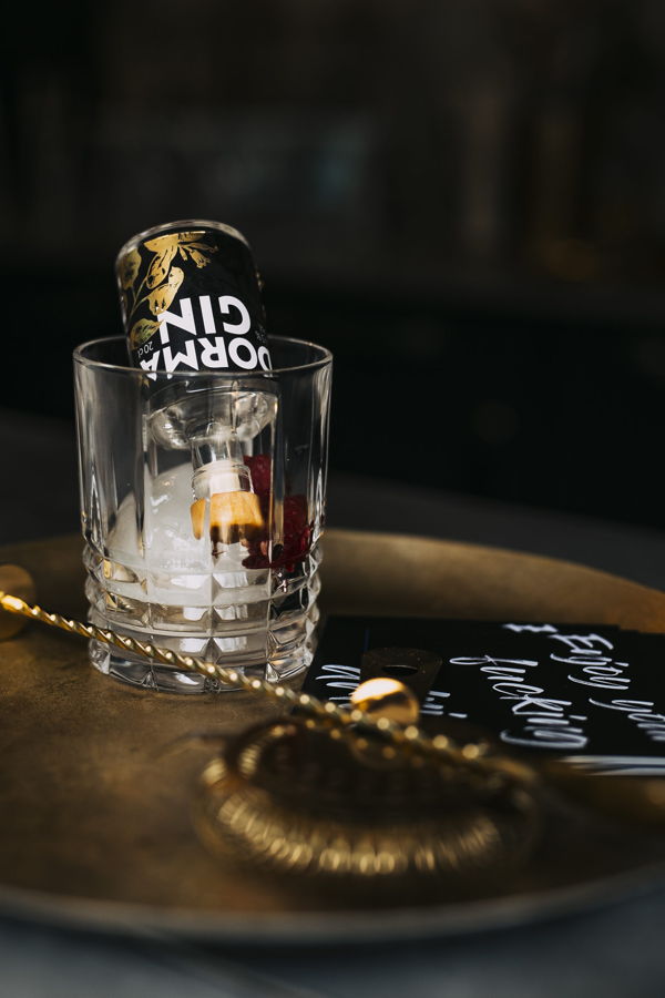 Glas mit Eiswürfeln und umgedrehter Gin-Dose auf einem Tablett