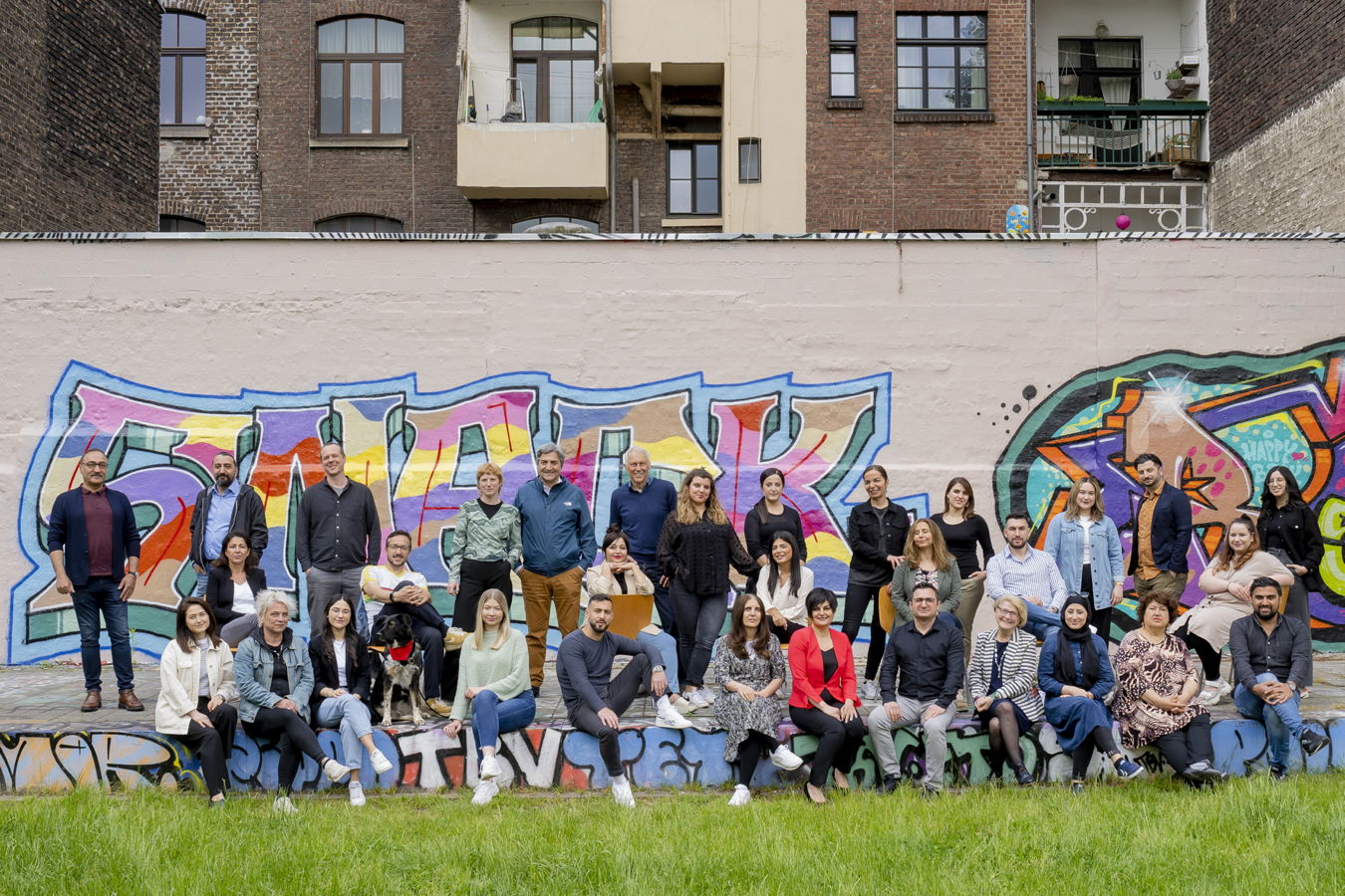 Gruppenfoto von 27 Personen vor einer bunten Graffiti-Wand