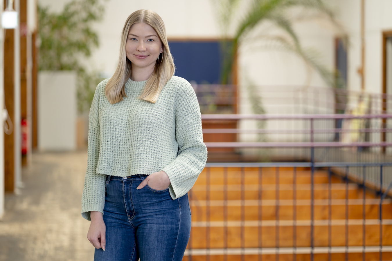Junge Frau in einem hellen Innenraum mit grünem Pullover und Jeans