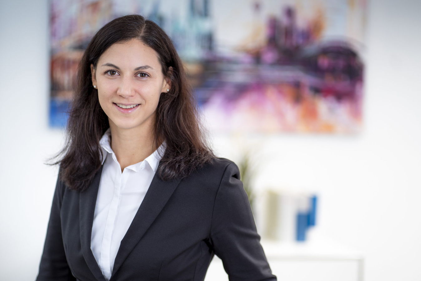 Porträt einer lächelnden Frau im Business-Outfit vor unscharfem Hintergrund