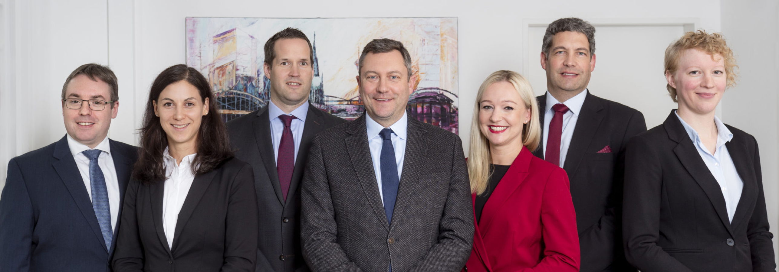 Sechs Personen in Businesskleidung stehen nebeneinander und lächeln in einem Büro