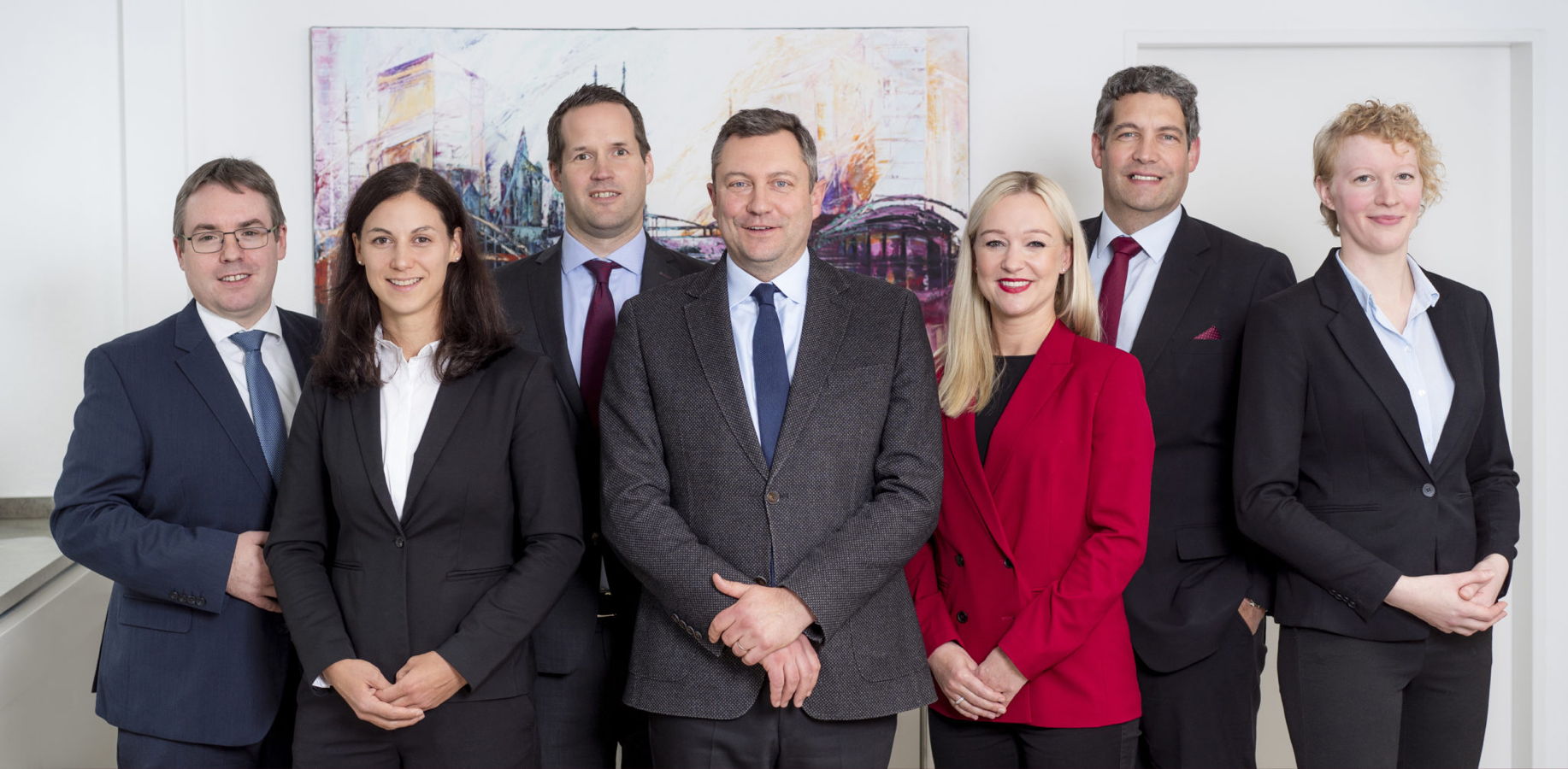 Gruppenfoto von sechs Geschäftsleuten in Anzügen vor einem Gemälde