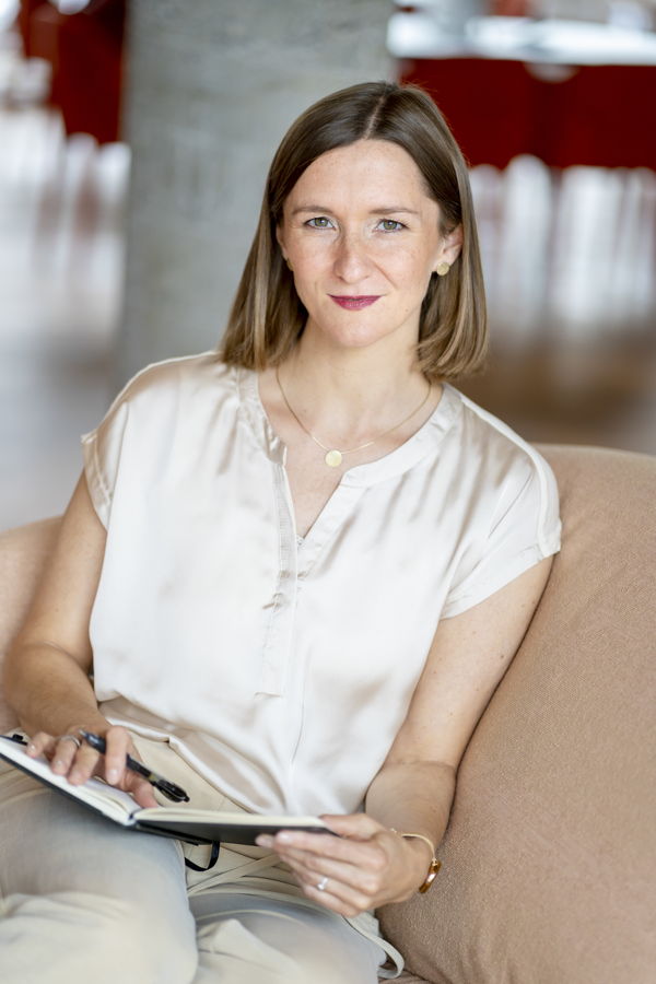 Frau sitzt auf einem Sofa und schreibt in ein Notizbuch