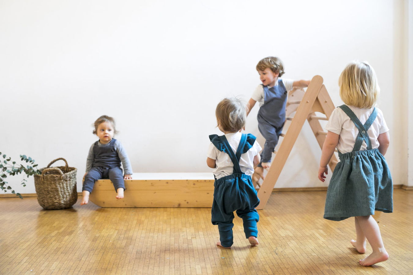 Vier kleine Kinder spielen in einem hellen Raum mit einem Klettergerüst aus Holz