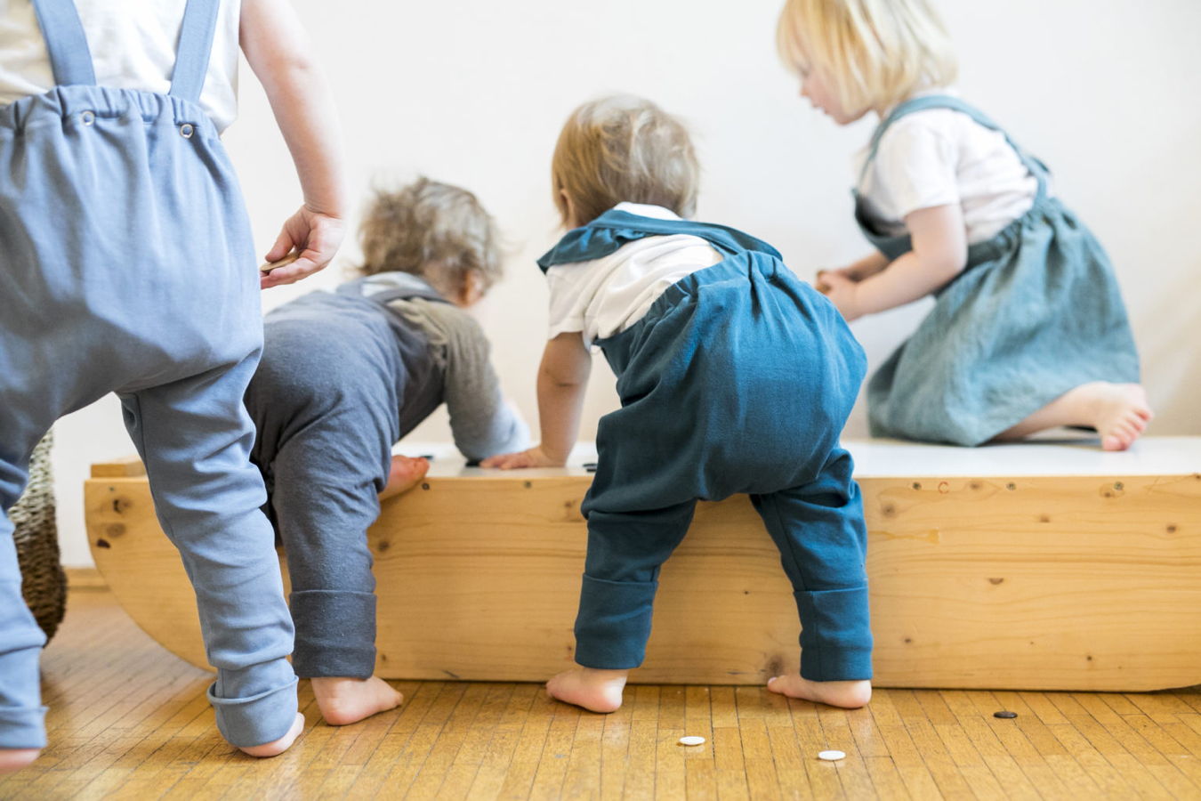 Mehrere Kleinkinder krabbeln auf einer Holzbank in einem hellen Raum