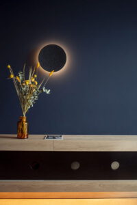 Vase mit Trockenblumen auf einer Holzkommode vor dunkelblauer Wand mit runder Wanddekoration