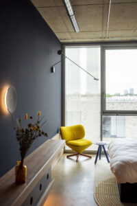 Modernes Schlafzimmer mit gelbem Sessel, großem Fenster und minimalistischem Interieur