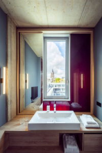 Modernes Badezimmer mit Waschbecken vor einem großen Spiegel und Blick auf die Stadt durch das Fenster