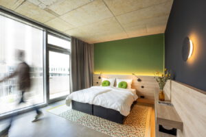 Modernes Hotelzimmer mit Doppelbett, grünem Akzent an der Wand und Balkonzugang