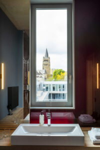 Badezimmer mit Waschbecken vor einem Fenster, durch das ein Kirchturm zu sehen ist